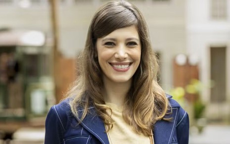 Caroline Dallarosa sorri e está com os cabelos soltos; ela usa um blazer azul com blusa bege por baixo