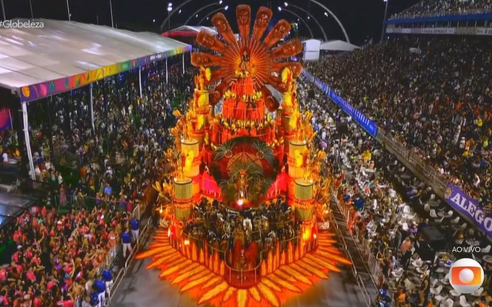 Um carro alegórico todo em cores vermelhas, amarelas e laranjas está na avenida do sambódromo do Anhembi