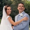 Vestida de noiva, Isis Valverde posa sorridente enquanto segura o braço de Marcus Buaiz, que veste um terno azul claro