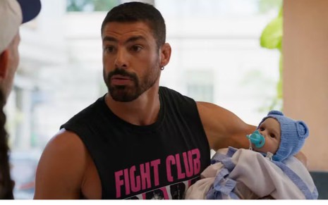 Cauã Reymond está segurando um bebê reborn, em imagem da novela Vale Tudo
