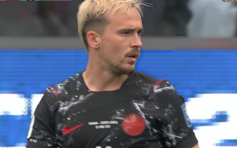 Liam Millar em campo, olhando para a direita, com a camisa vermelha, azul e preta do Canadá