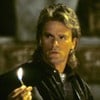 Richard Dean Anderson segura um fósforo aceso em cena da série MacGyver - Profissão: Perigo; ele tem mullet no cabelo, com visual típico dos anos 1980