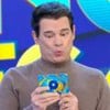 Celso Portiolli faz biquinho enquanto segura microfone e uma ficha no Passa ou Repassa