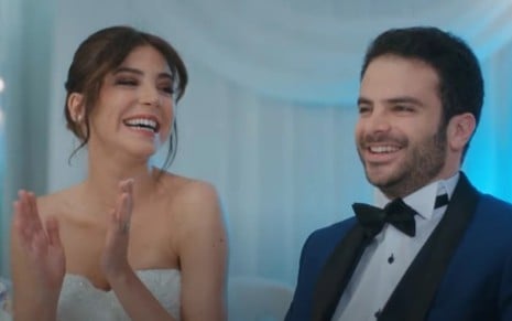 Os atores Gökçe Eyüboğlu e Sinan Helvac vestidos de noivos, sorrindo, em cena de Força de Mulher