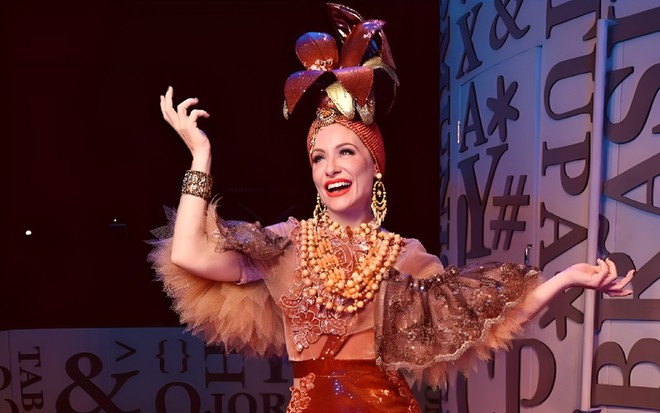 Caracterizada como Carmen Miranda, Giselle De Prattes faz pose no palco de um teatro