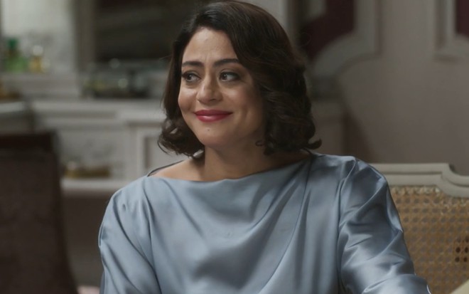 A atriz Carol Castro com leve sorriso de boca fechada, em cena de Garota do Momento