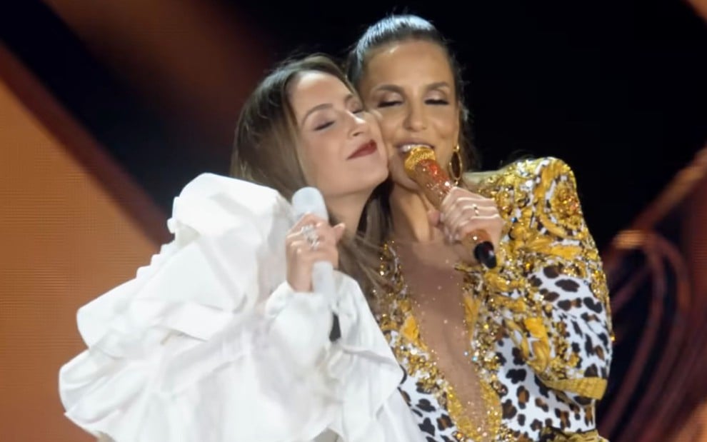 Claudia Leitte e Ivete Sangalo com os rostos colados enquanto cantam