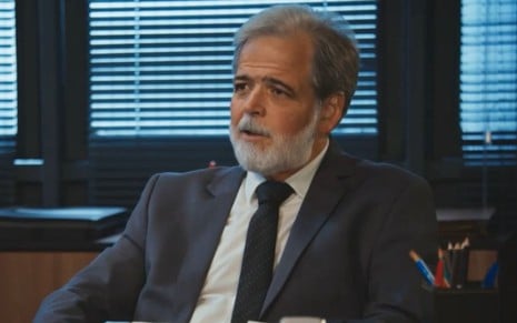 Claudio Cinti sentado em uma mesa de delegacia em cena da novela Família É Tudo