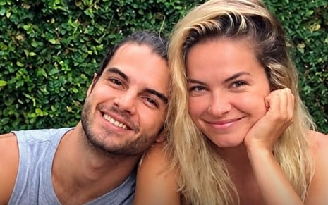Um homem está ao lado esquerdo de uma mulher loira, com a cabeça me seu ombro, ambos sorridentes