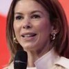 Daniela Beyruti fala em um microfone em frente a um fundo vermelho