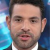 Três jornalistas aparecem lado a lado em estúdio, usando trajes formais e microfones.