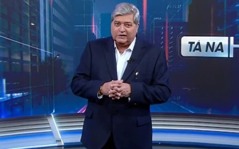 O apresentador José Luiz Datena, com as mãos cruzadas, no cenário do Tá na Hora