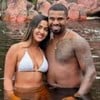 Adriana Paula e Davi Brito estão abraçados, com metade do corpo submerso em um rio e roupas de banho