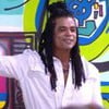 Diogo Almeida se despede de participantes no BBB 25; ele usa camisa branca, tem dreads no cabelo e está com o braço direito levantado