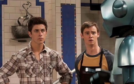 David Henrie e Dan Benson parecem compenetrados enquanto observam robô em cena de Os Feiticeiros de Waverly Place