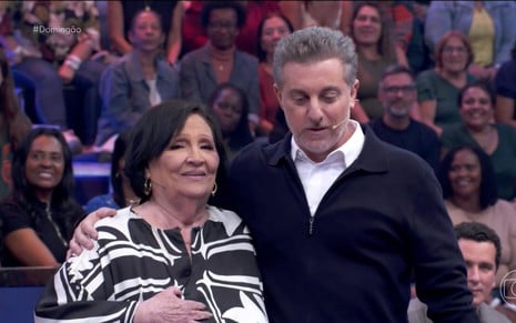 Dona Déa Lúcia e Luciano Huck no Domingão com Huck deste domingo, ela com expressão emocionada e ele olhando para baixo