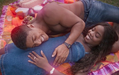 Os atores Humbeto Morais e Clara Moneke deitados, sorrindo, ele com a mão na barriga dela em cena de Dona de Mim