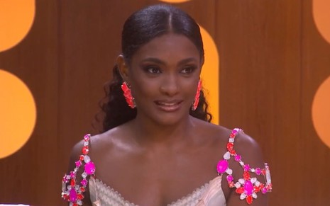 Erika Januza está com cabelo preso em rabo de cavalo baixo, usa uma regata rosa e brincos de pedraria
