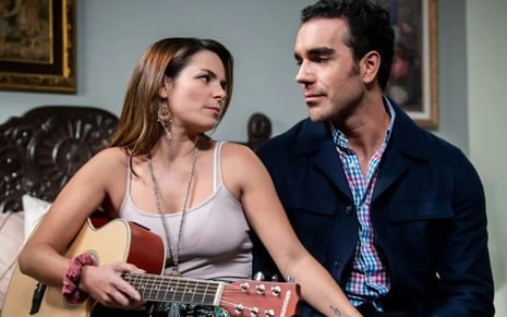 Os atores Alejandra Robles Gil e Marcus Ornellas na novela Eternamente Apaixonados, se olhando, sérios, ela com violão no colo