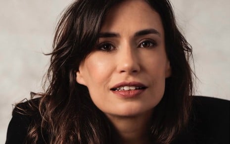 Fernanda Chicolet: mulher branca, de cabelo castanho-escuro, posando em frente a um fundo branco com roupas pretas