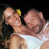 Fernanda Lima e Rodrigo Hilbert abraçados e sorridentes na véspera de Ano-Novo; os dois vestem branco e ela usa uma flor amarela no cabelo