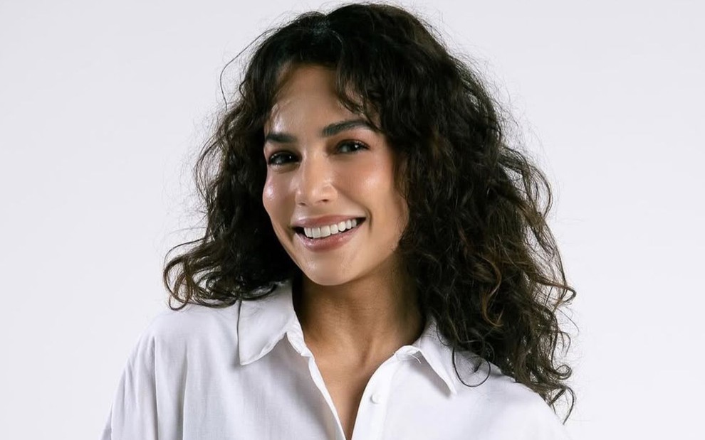 Fernanda Marques sorri e está com os cabelos longos soltos; ela usa uma camisa branca