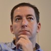 Glenn Greenwald tem expressão séria, com a mão no queixo