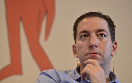 Glenn Greenwald tem expressão séria, com a mão no queixo