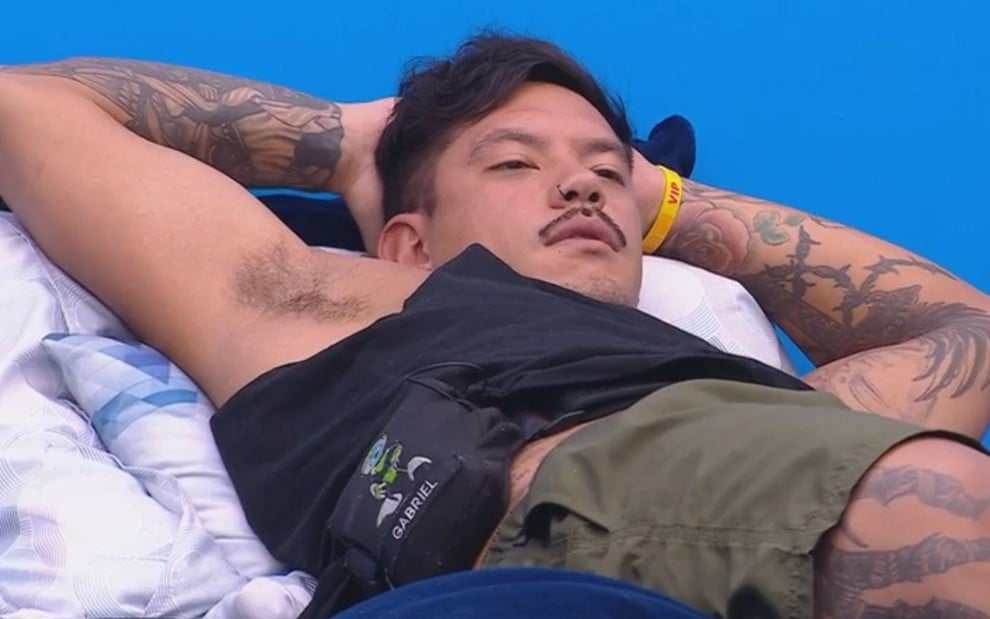 Gabriel Yoshimoto está deitado em cama do BBB 25 e coloca os dois braços atrás da cabeça