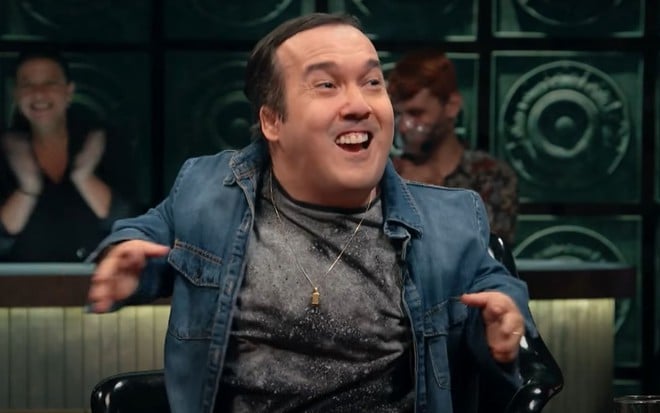 Gigante Leo no Que História É Essa, Porchat?, sentado com uma camisa jeans, e rindo
