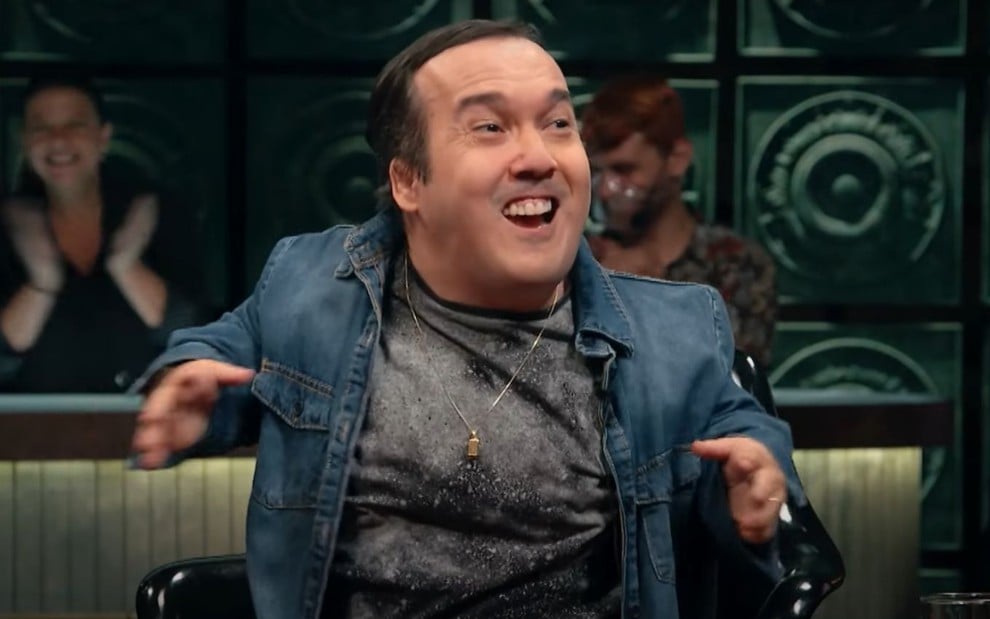 Gigante Leo no Que História É Essa, Porchat?, sentado com uma camisa jeans, e rindo