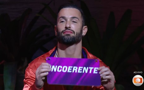 Diego Hypolito mostra plaquinha com a palavra "incoerente" na área externa do BBB 25