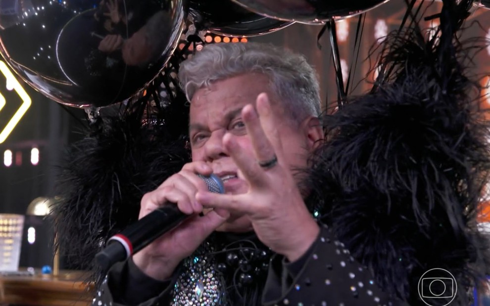 Milton Cunha usa terno preto com plumas e bexigas amarradas no palco do Domingão com Huck