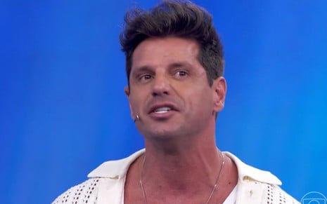 O apresentador Fernando Fernandes em frente a um fundo azul no palco do Domingão com Huck