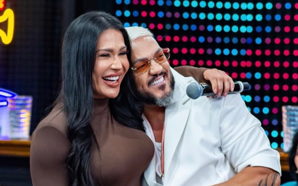 Gracyanne Barbosa e Belo posam sorridentes e abraçados no palco do Domingão