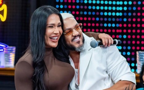Gracyanne Barbosa e Belo posam sorridentes e abraçados no palco do Domingão