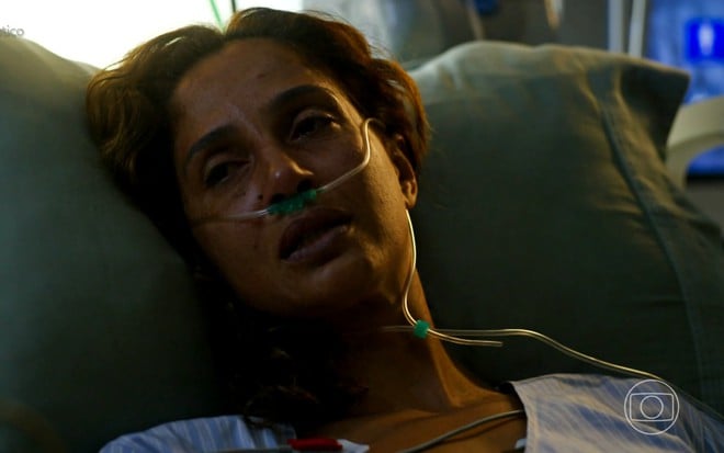 Camila Pitanga tem aparência doente e está deitada em uma cama de hospital, com canudos enfiados no nariz