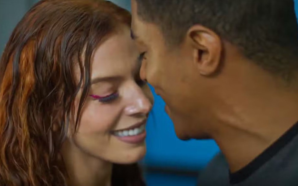 Casal sorri e se aproxima para um beijo; mulher usa delineado rosa e cabelo molhado, clima de intimidade e romance.