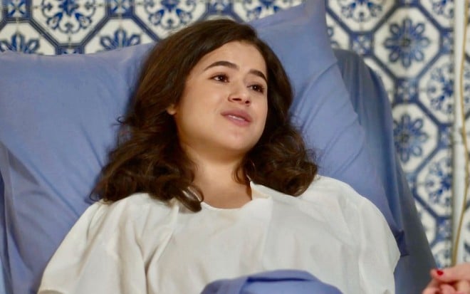 A atriz Maisa deitada em cama de hospital em cena de Garota do Momento