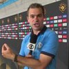 Repórter da Globo gesticula enquanto fala ao microfone em frente a painéis com logotipos da Copa do Mundo de Clubes da Fifa.