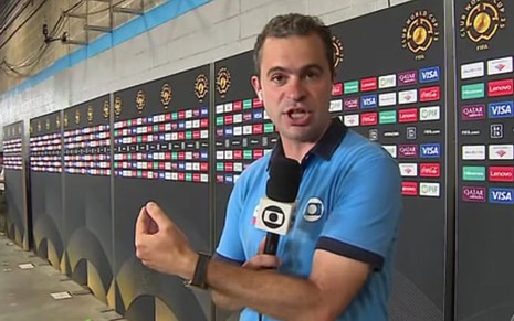 Repórter da Globo gesticula enquanto fala ao microfone em frente a painéis com logotipos da Copa do Mundo de Clubes da Fifa.