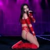 Anitta de vermelho, ajoelhada, cantando