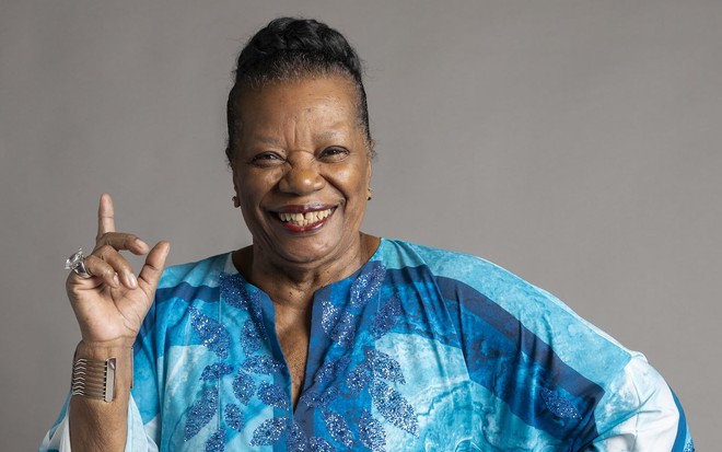 A atriz Neusa Borges posa com vestido azul e dedo levantado