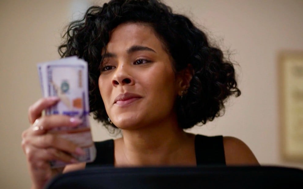 Bella Campos como Maria de Fátima segura maço de dólares no remake de Vale Tudo, da Globo