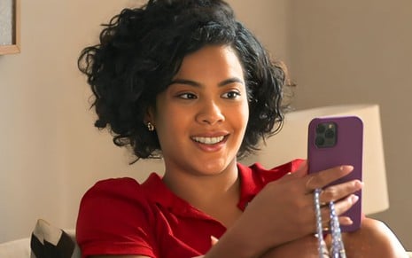 A atriz Bella Campos segura um Iphone como a Maria de Fátima em cena de Vale Tudo