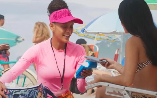 A atriz Taís Araujo como Raquel vendendo sanduíche na praia em cena de Vale Tudo