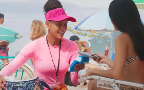 A atriz Taís Araujo como Raquel vendendo sanduíche na praia em cena de Vale Tudo