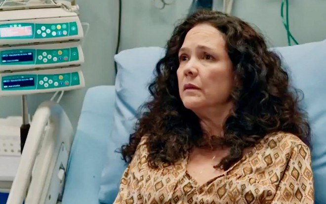 A atriz Tereza Seiblitz com expressão séria, em cama de hospital, em cena de Volta por Cima