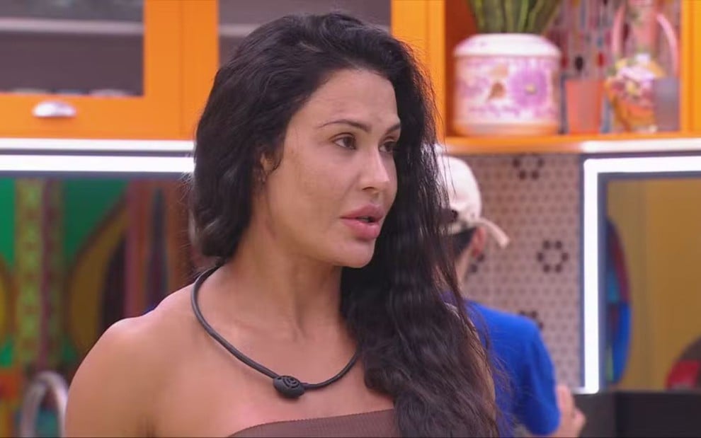 Gracyanne Barbosa na cozinha do BBB 25, com olhar indignado, enquanto usa um top marrom e o cabelo está jogado para o lado esquerdo