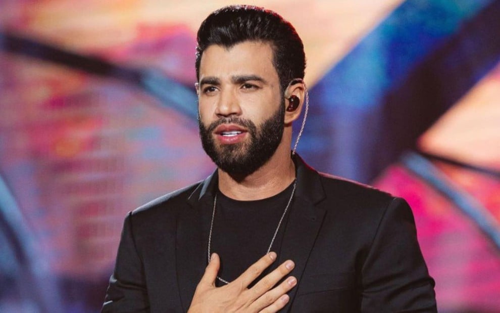 Gusttavo Lima está com a mão no peito em seu show